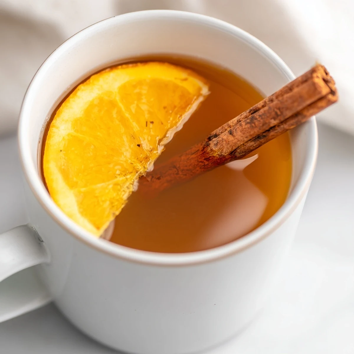 A close-up of amber cider spiced apple cider, garnished with a vibrant orange slice.