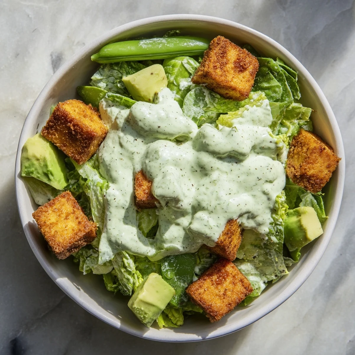 Close-up of crispy baked tofu cubes with golden edges, served on a vibrant Green Goddess Salad with romaine, cabbage, cucumber, avocado, and snap peas.