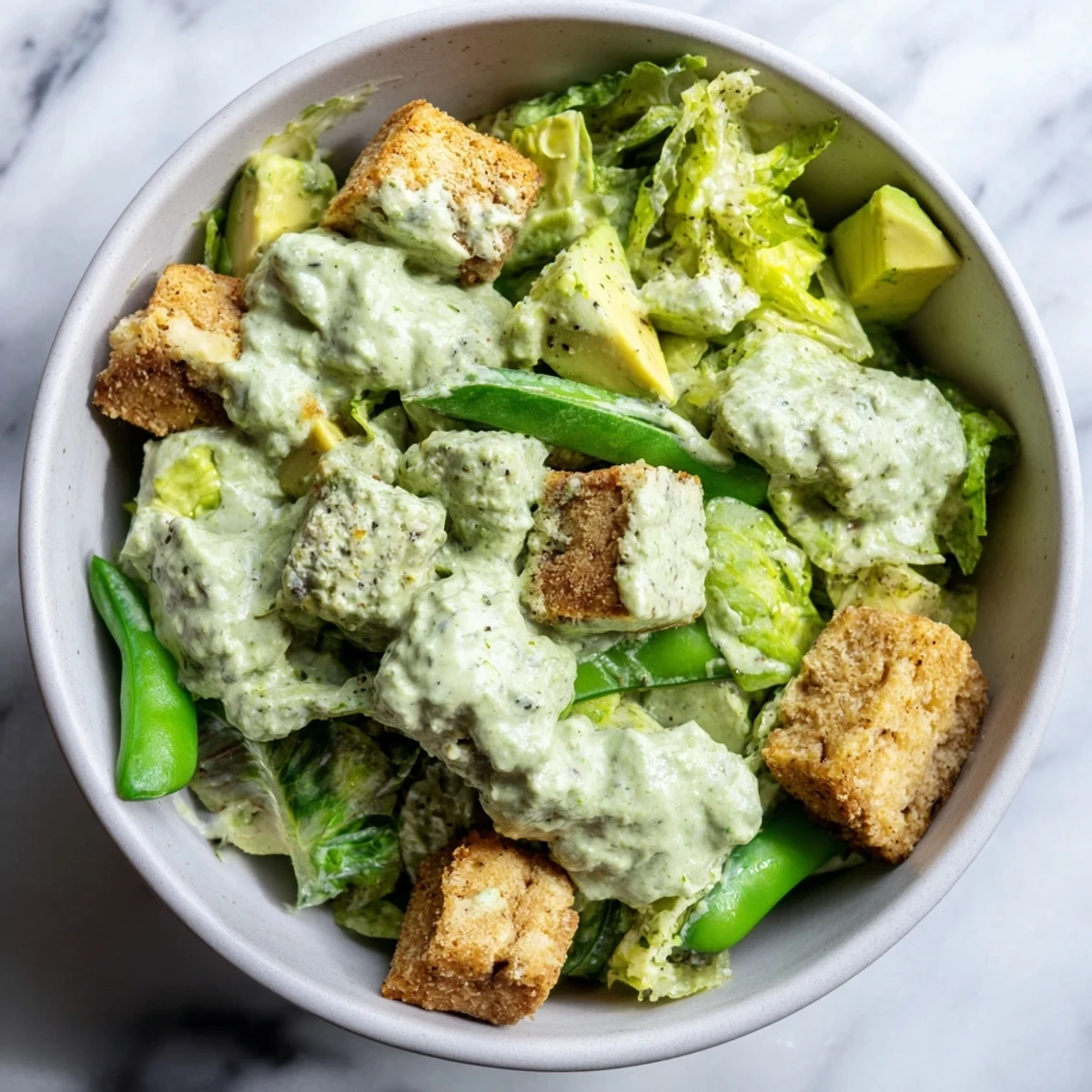 The finished Green Goddess Salad with Baked Tofu in a white bowl, topped with fresh herbs and creamy green goddess dressing on the side.