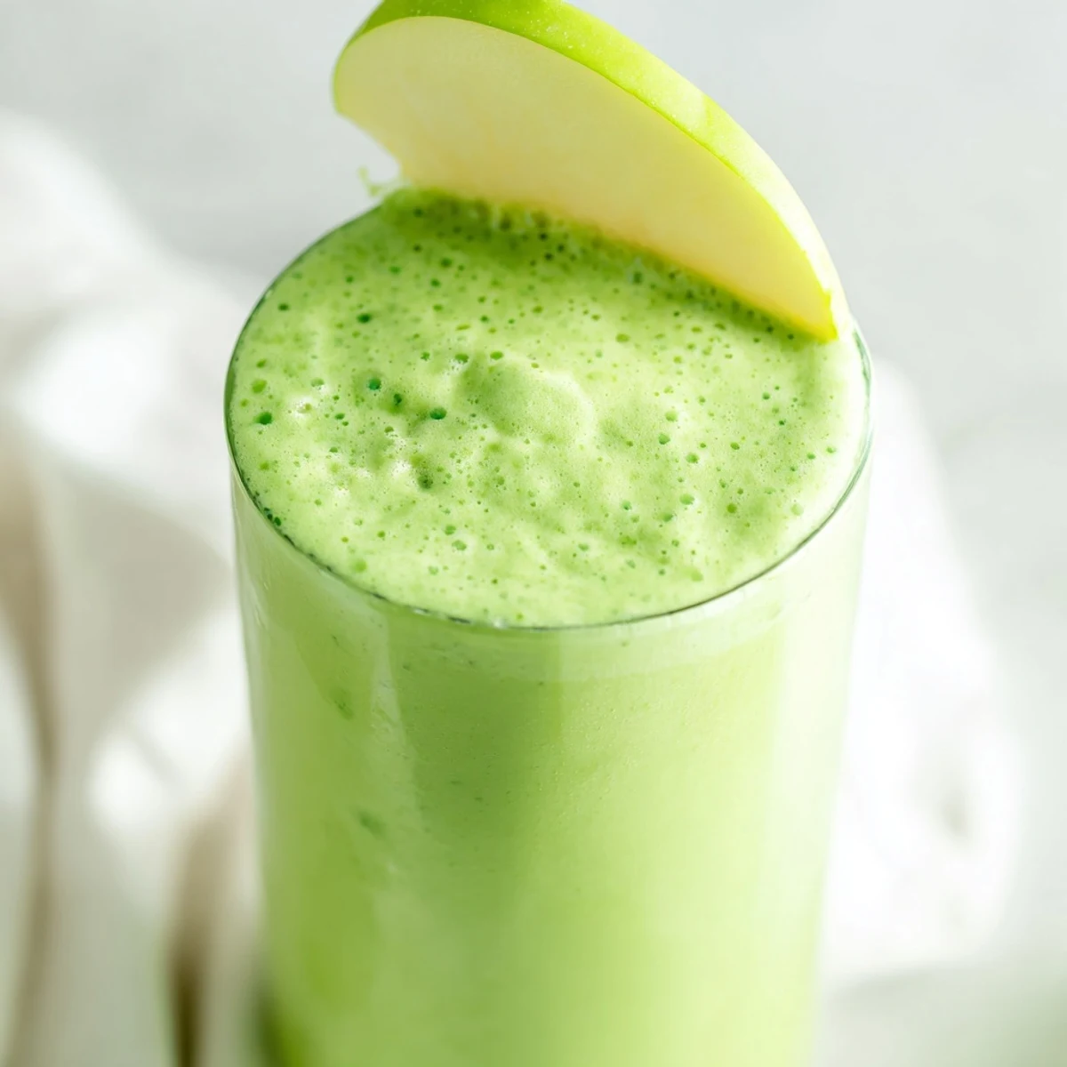 A tall glass of Detox Green Smoothie garnished with ginger and apple slices, ideal for a healthy breakfast.