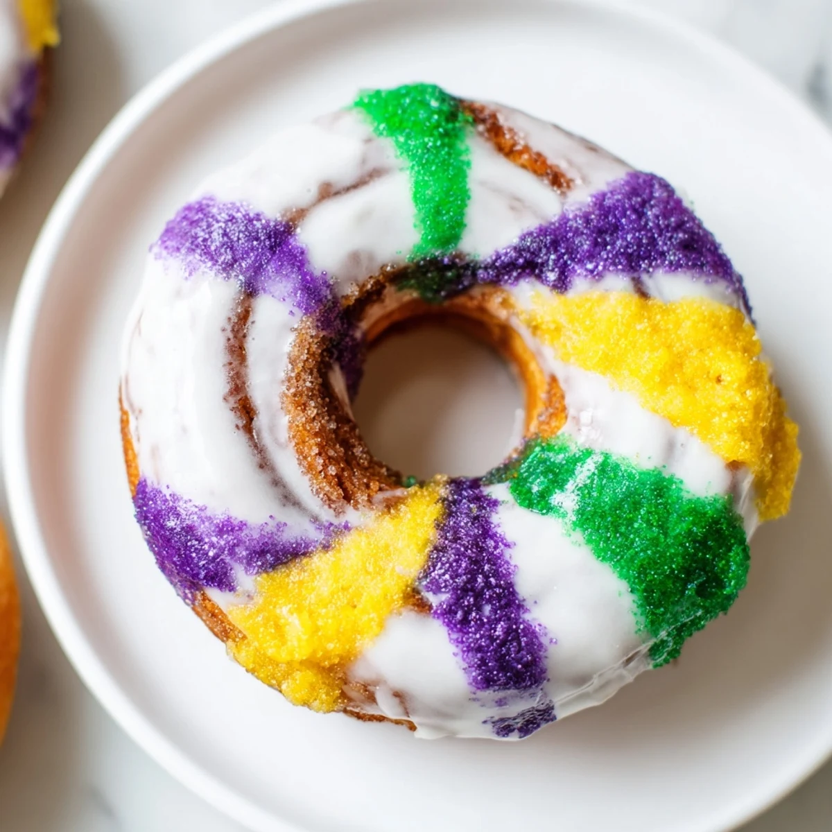 Golden Mardi Gras King Cake Donuts on a platter, swirled with cinnamon sugar and generously topped with vibrant Mardi Gras colored sprinkles.
