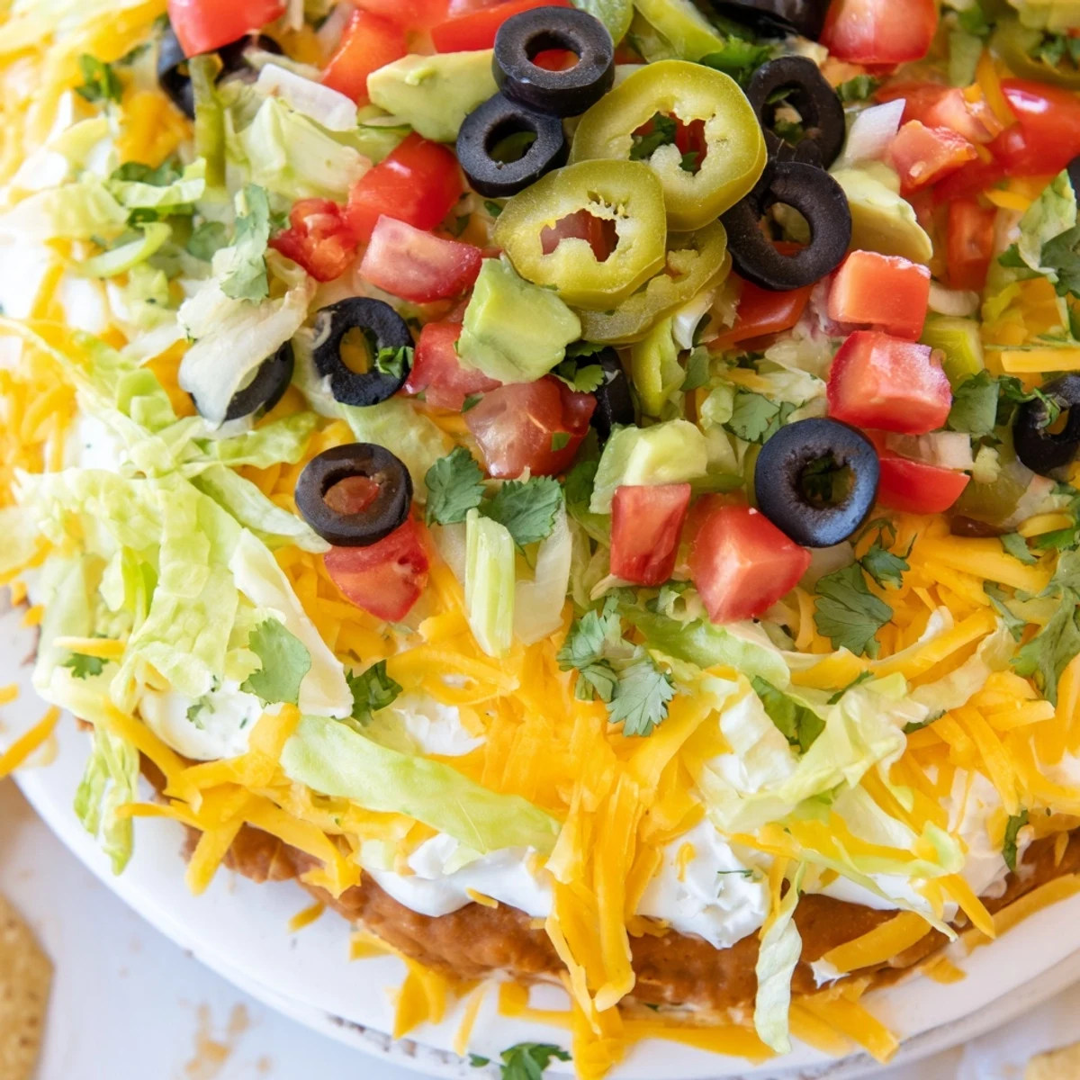 A chilled Ultimate Layered Taco Dip topped with olives, tomatoes, and cheese for a party.