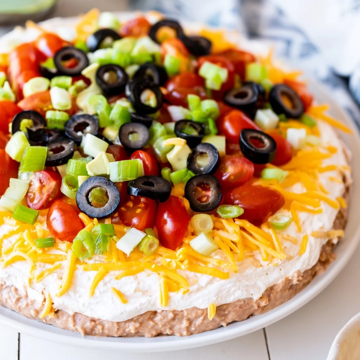 Ultimate Layered Taco Dip in a clear glass dish, showcasing distinct layers and colorful garnishes, ready to be served.