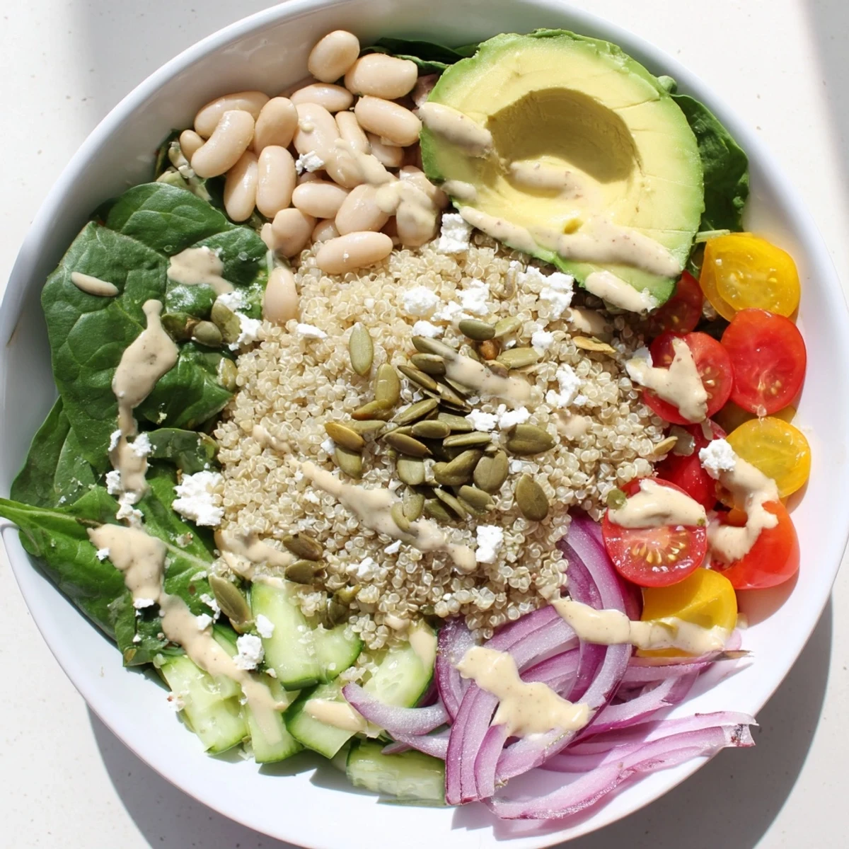 Colorful Spinach & White Bean Ultimate Protein Power Bowl with quinoa, fresh spinach, cherry tomatoes, and cucumber in a white ceramic bowl.