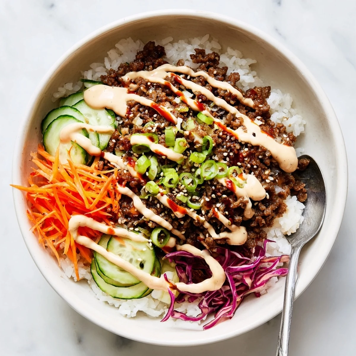 A close-up of a Korean Beef Bowl with Spicy Mayo, featuring fluffy rice topped with savory beef, crunchy carrots, and a creamy drizzle.