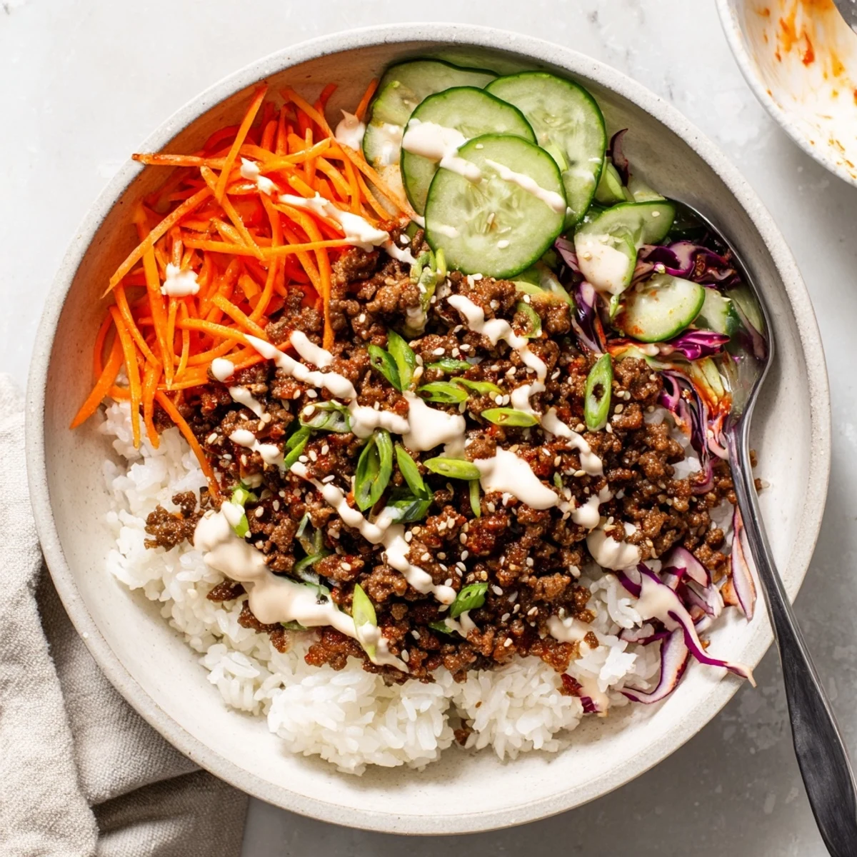 In this Korean Beef Bowl with Spicy Mayo, vibrant cucumbers and red cabbage add crisp texture to the warm, savory ground beef over rice.
