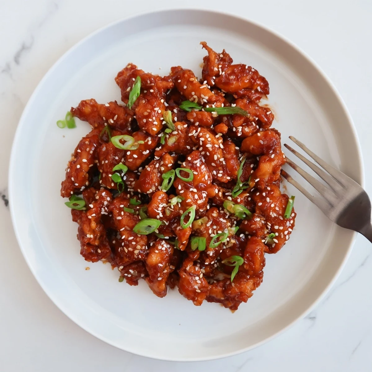 Shredded slow cooker sesame chicken served over white rice with fresh green onion sprinkles on top