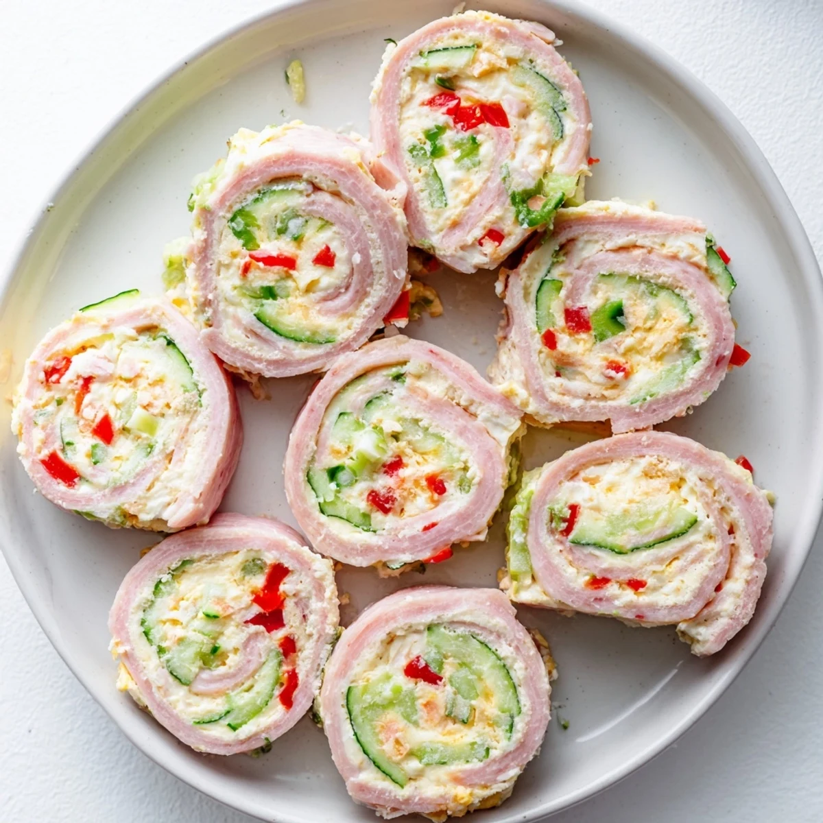 Low-carb keto ham roll ups arranged on a serving platter showcasing the rolled deli ham with bright bell pepper and cucumber ribbons peeking through