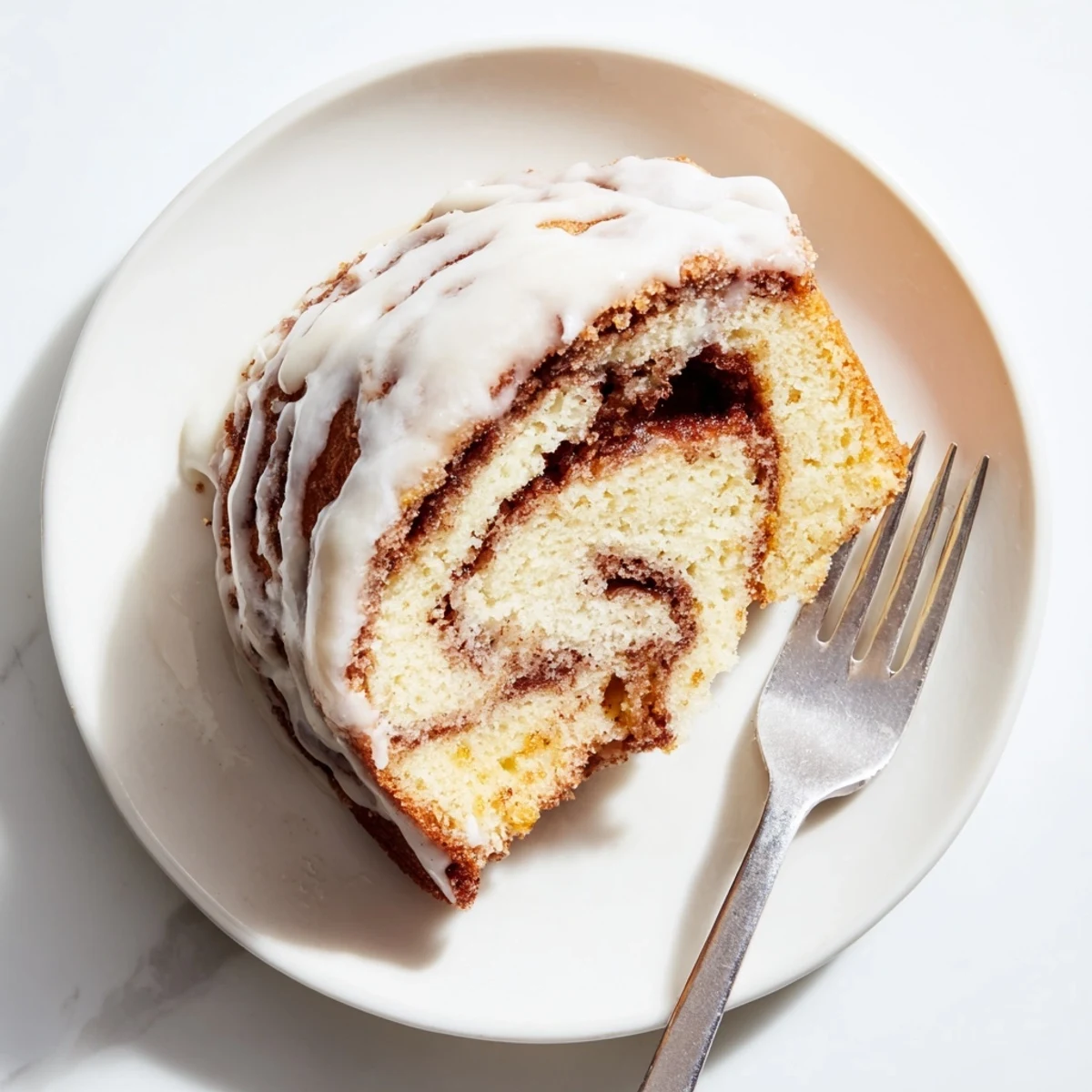 Soft buttery cinnamon roll cake slice displaying spiraled cinnamon ribbons beneath a sweet powdered sugar glaze