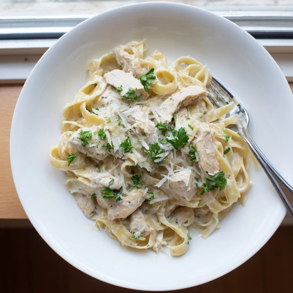 Golden brown chicken pieces atop fettuccine noodles coated in savory parmesan garlic cream sauce with fresh parsley garnish