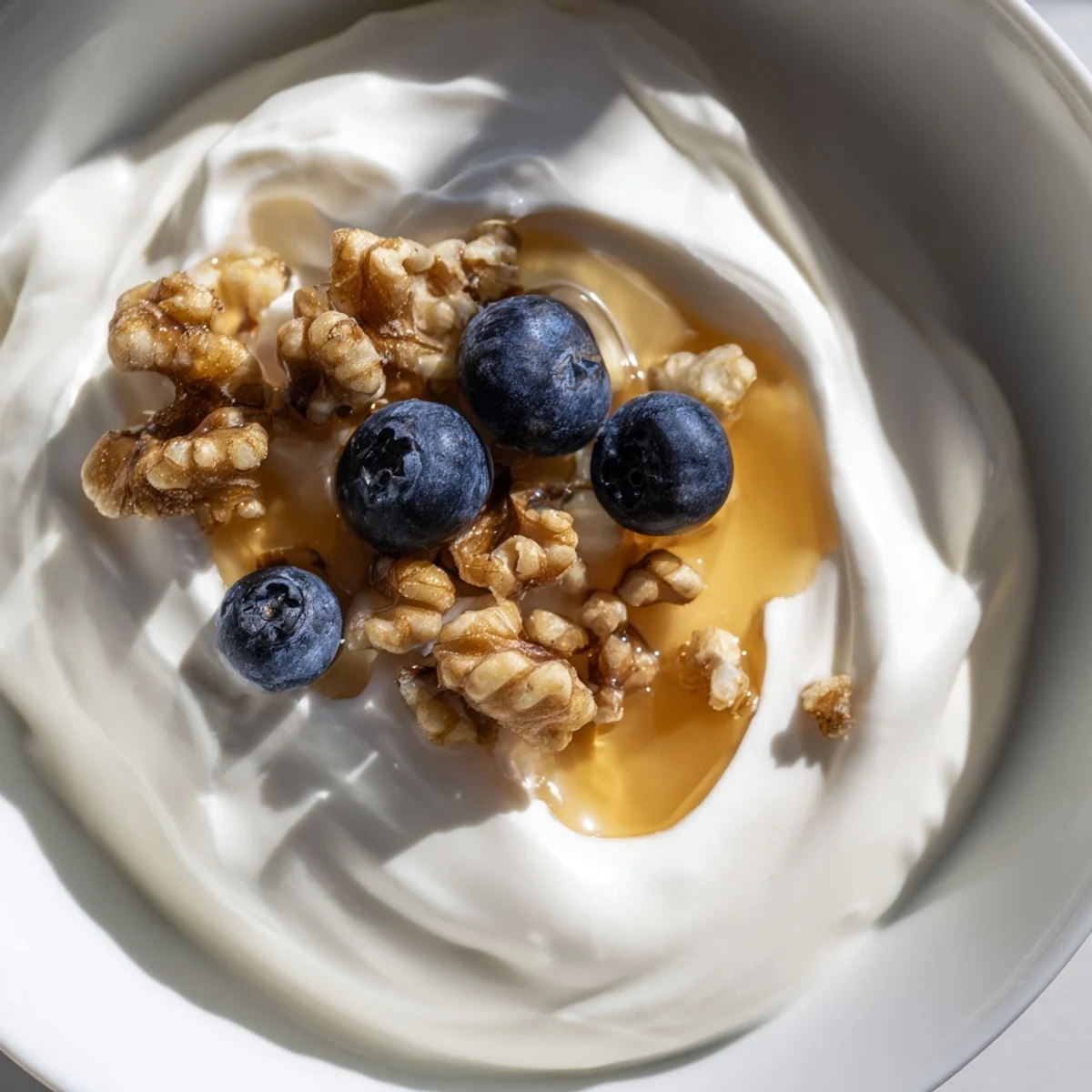 Glass jar filled with tangy homemade Greek yogurt surrounded by milk and honey