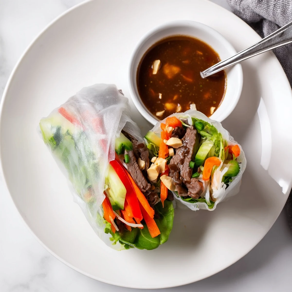 Plate of Thai Basil Beef Rolls halved, peanut-hoisin sauce pooled nearby.