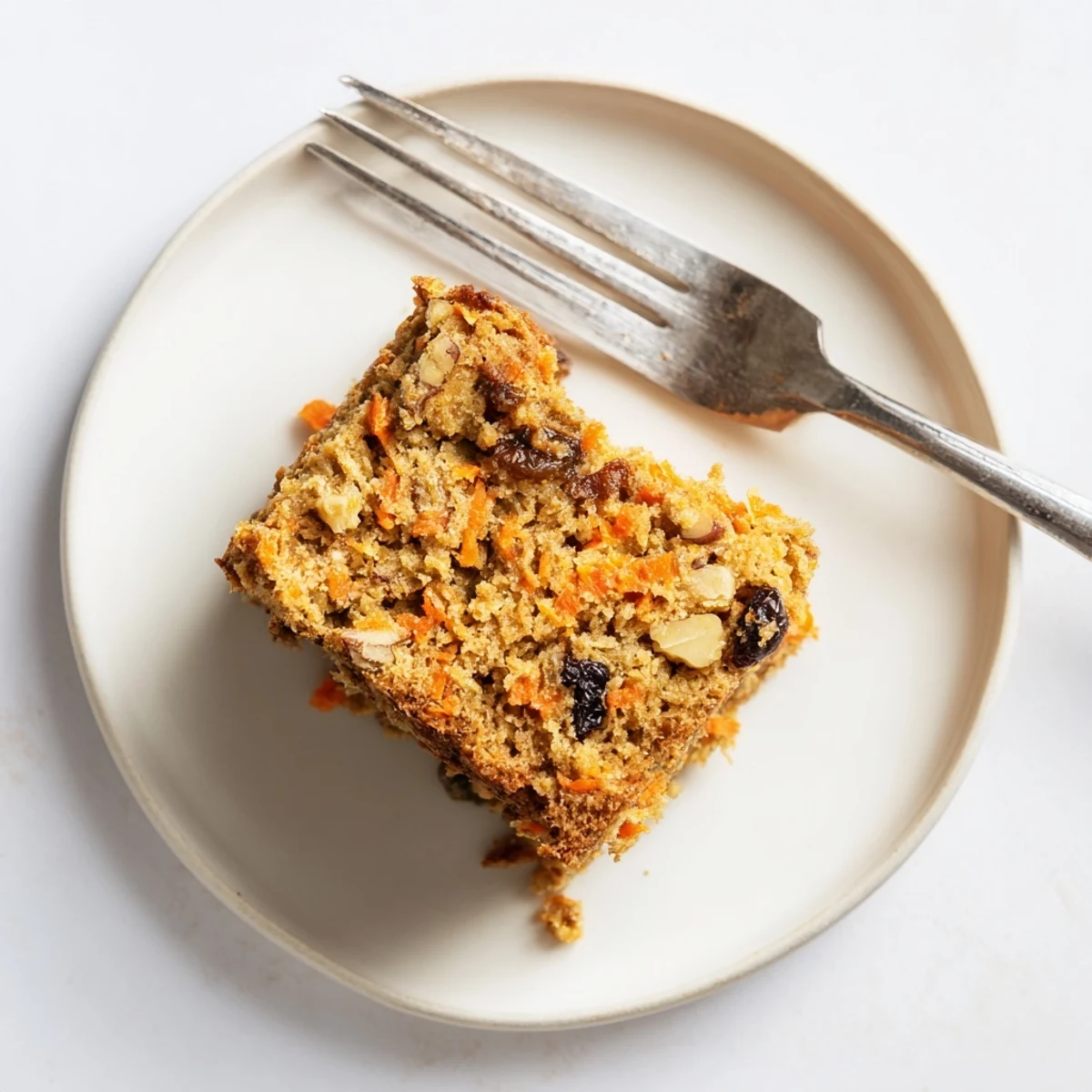 Moist flourless oatmeal carrot cake slice topped with chopped walnuts on a white plate