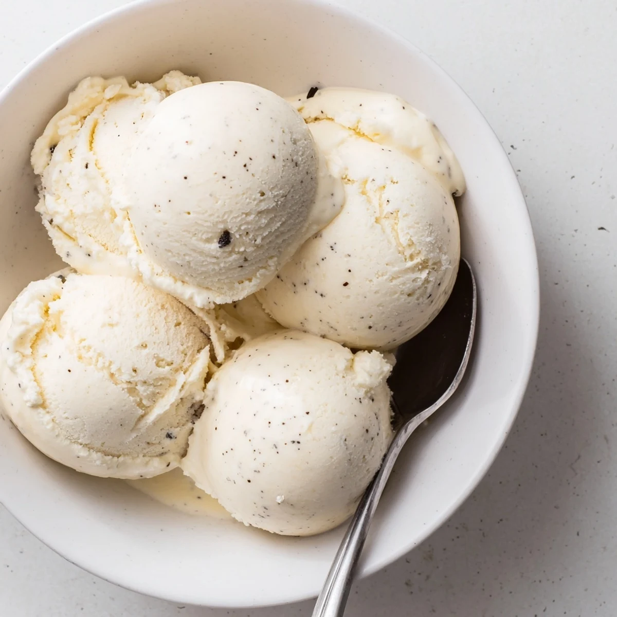 Rich vanilla bean ice cream scooped into a vintage dessert dish with chocolate sauce