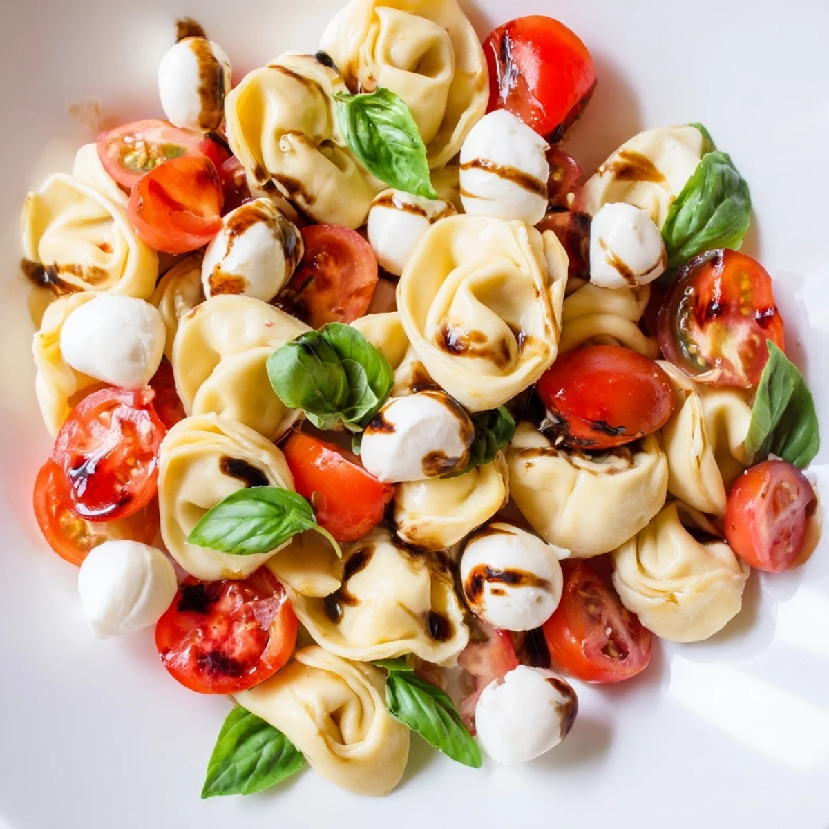 Fresh Italian pasta salad showcasing al dente cheese tortellini tossed with halved grape tomatoes, basil, and bocconcini in olive oil dressing