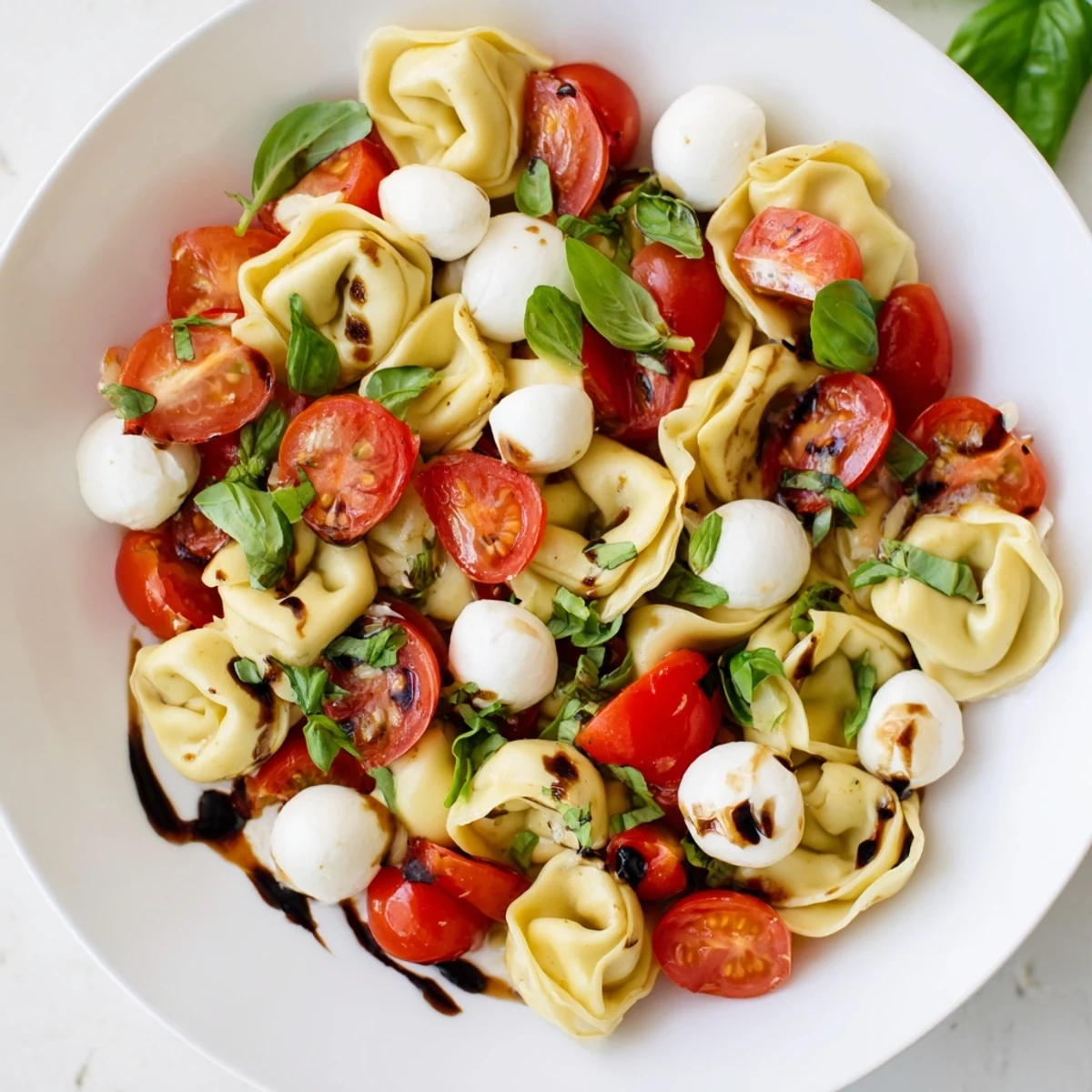 Vibrant summer plate of tortellini Caprese salad with tender cheese pasta, ripe cherry tomatoes, and fresh basil finished with tangy balsamic reduction