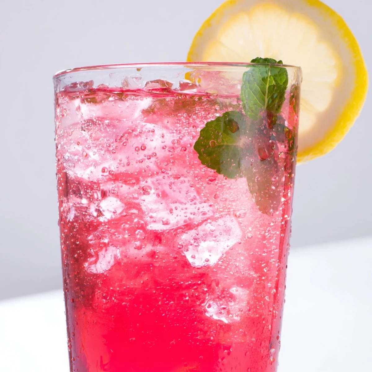 Sparkling honey lemon pink soda poured over ice with vibrant grapefruit tones and a delicate mint sprig for a refreshing summer mocktail